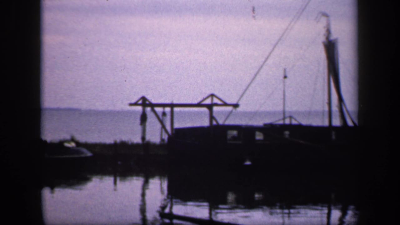 Moored boat and crane-like dock structure silhouetted beside calm water.
