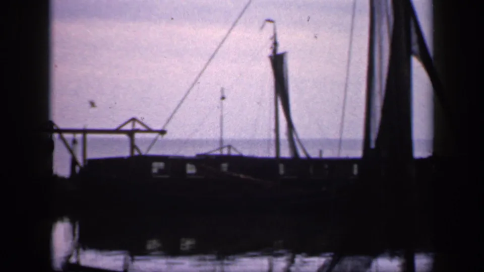 1949 Ireland dockside frame with a silhouetted vessel, upright mast, crane-like structure, and still harbor water.