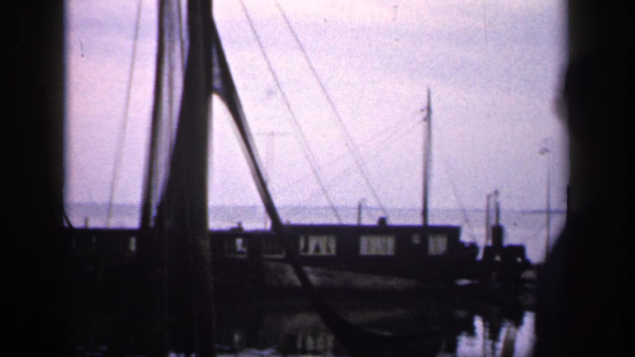 Dark harbor or waterfront view with masts, water, and silhouetted structures.