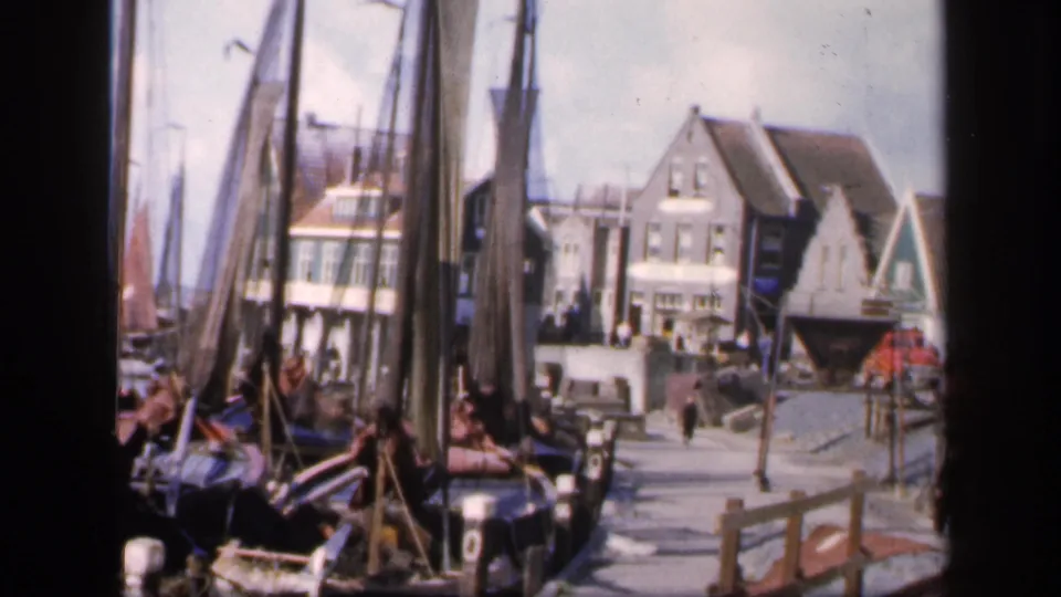 1949 Ireland harbor view with sailboat masts in the foreground, people on the quay, and gabled buildings along the waterfront.