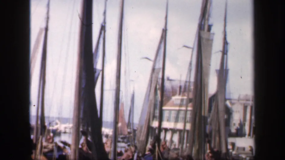1949 Ireland harbor view with sailboat masts, furled sails, quay lamps, a waterfront building, and open water beyond.