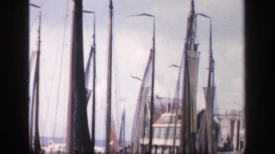 1949 Ireland 8mm still with moored sailboats, mast lines, a pale harbor building, distant water, and a bright overcast sky.