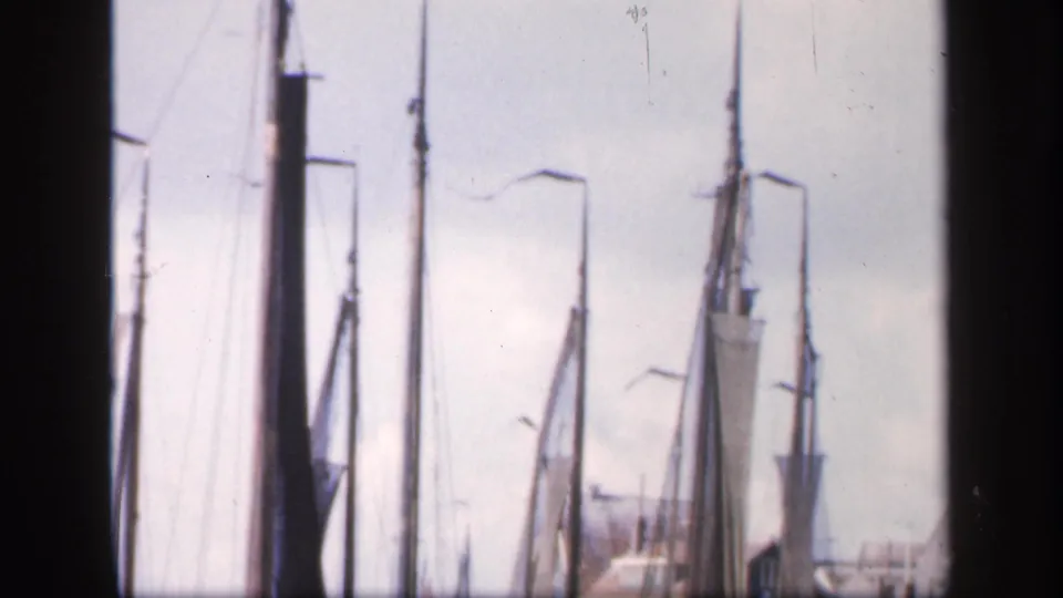 1949 Ireland harbor frame showing furled sailboats, tall masts, rigging, quay lamps, and waterfront buildings in soft 8mm color.