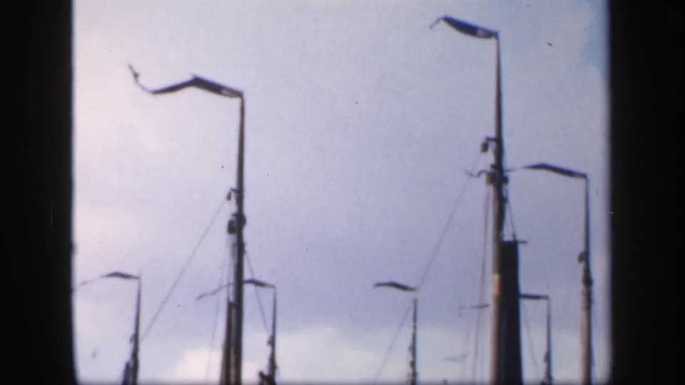 1949 Ireland 8mm frame showing sailboat masts, furled sails, rigging, and dock lamps against a pale cloudy sky.