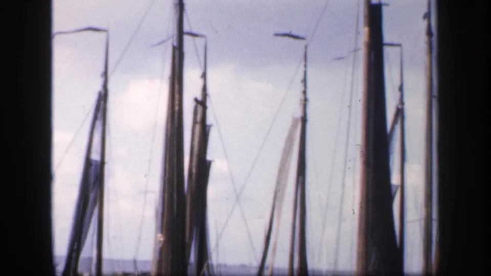 1949 Ireland frame showing clustered sailboat masts, furled sails, thin rigging, dock lights, and cloudy sky in faded 8mm color.