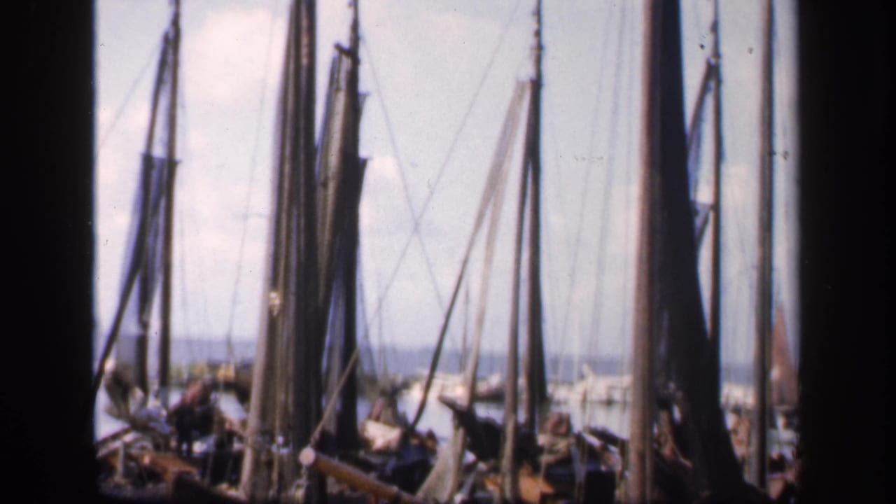 Crowded sailboats at a dock with tall masts, rigging, and small people near the boats.