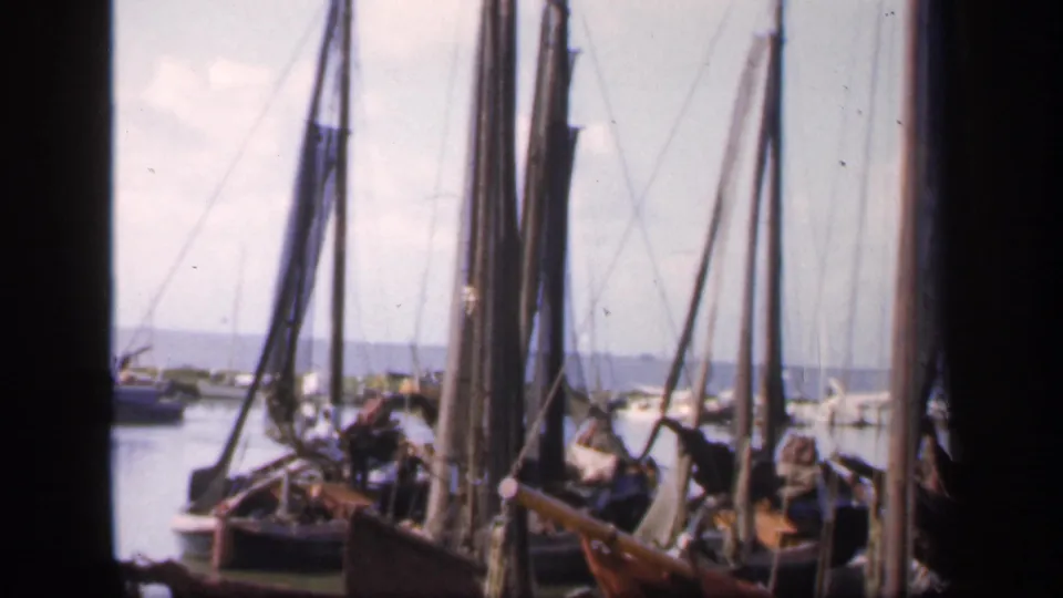 1949 Ireland 8mm view of moored sailing boats, rigging, calm water, and distant people near a quiet harbor dock.