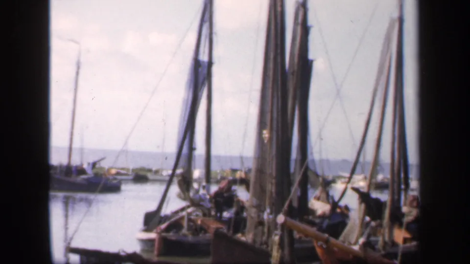 1949 Ireland harbor frame showing docked sailing boats and rigging in soft 8mm color, with calm water and land in the distance.