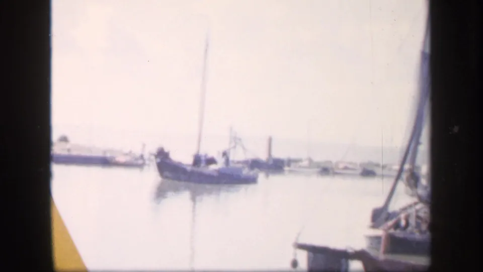 Bright 1949 Ireland harbor frame with a small boat on pale water, moored craft in the distance, and sailboat rigging at the edge.
