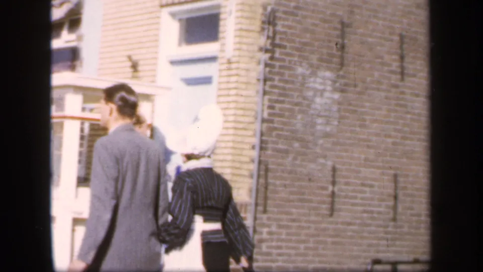 The pair walks away along a brick-lined street, with the woman’s white bonnet and striped dress visible beside the suited man.