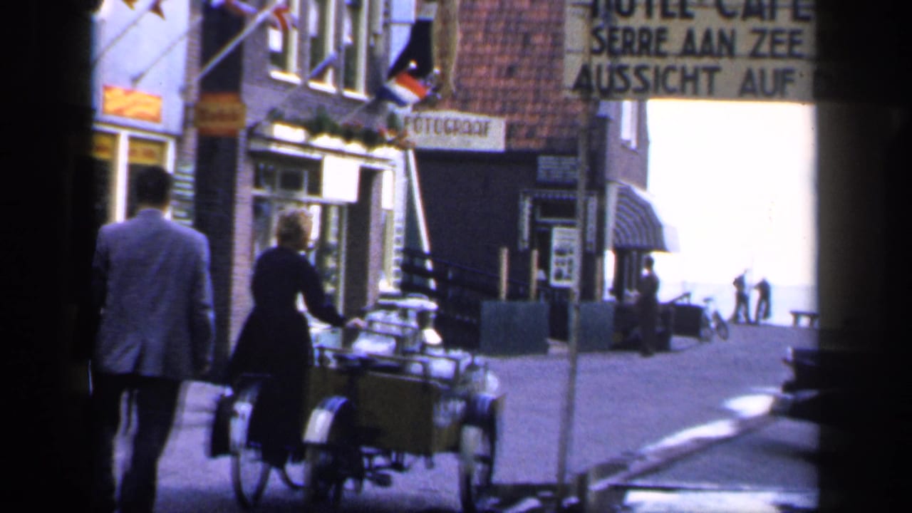 Man and woman walk along a narrow street beside a bicycle with a large cargo basket.