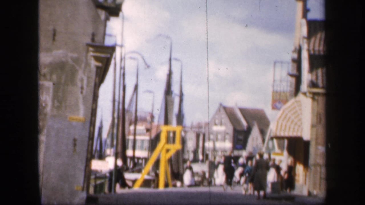 A group of women in white aprons and bonnets approaches on the street near pedestrians and bicycles.