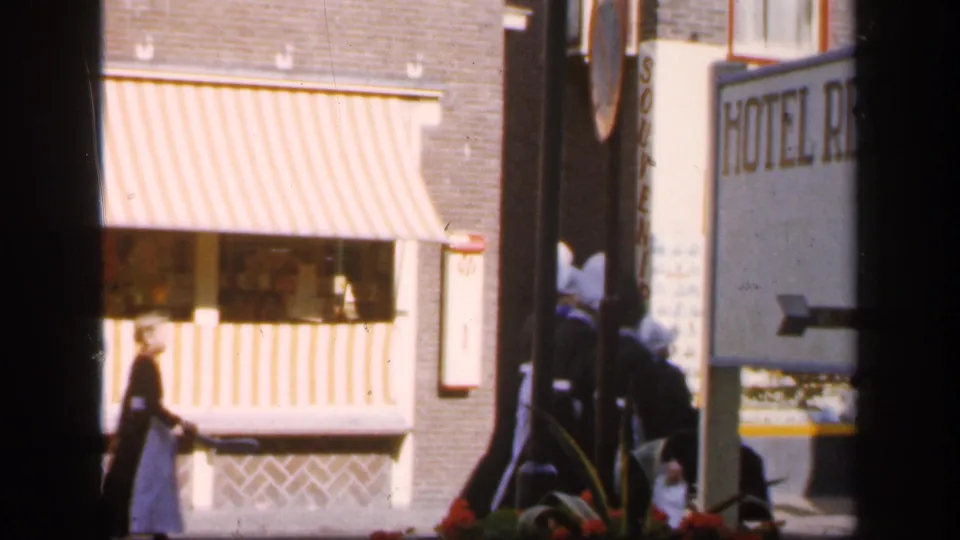 1949 Ireland home-movie frame showing a pedestrian by a striped storefront awning, flower display, and partial hotel sign.
