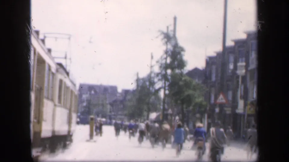 1949 Ireland home-movie street view with pedestrians, cyclists, buildings, and a large vehicle at the edge of frame.