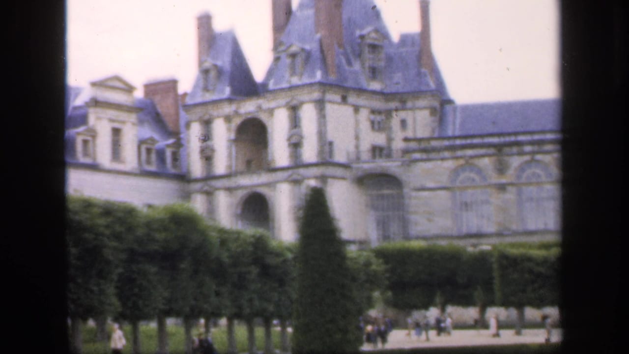 Grand chateau facade seen beyond clipped hedges and garden paths with small visitors below.