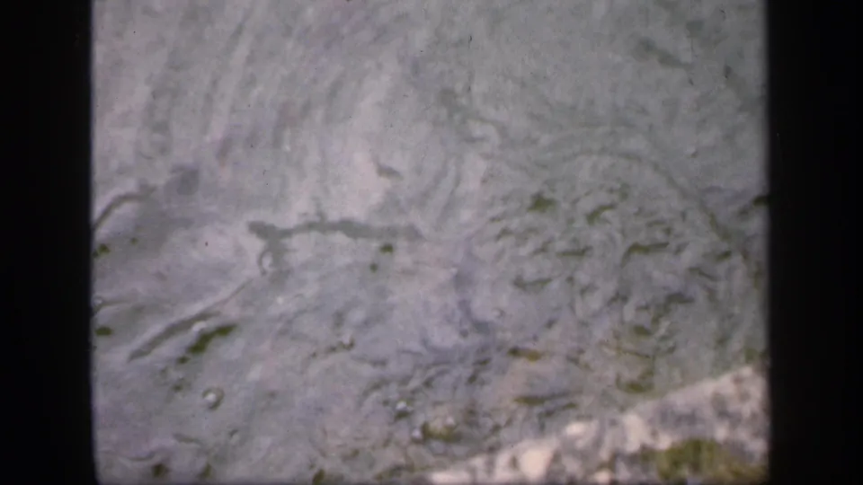 1949 Ireland home-movie still of cloudy rippled water with faint fish movement near the surface.