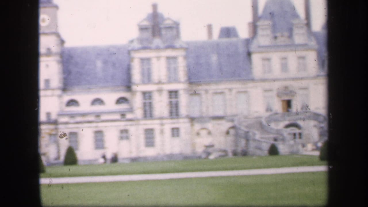 Soft 8mm view of a grand palace facade with lawn and distant visitors.