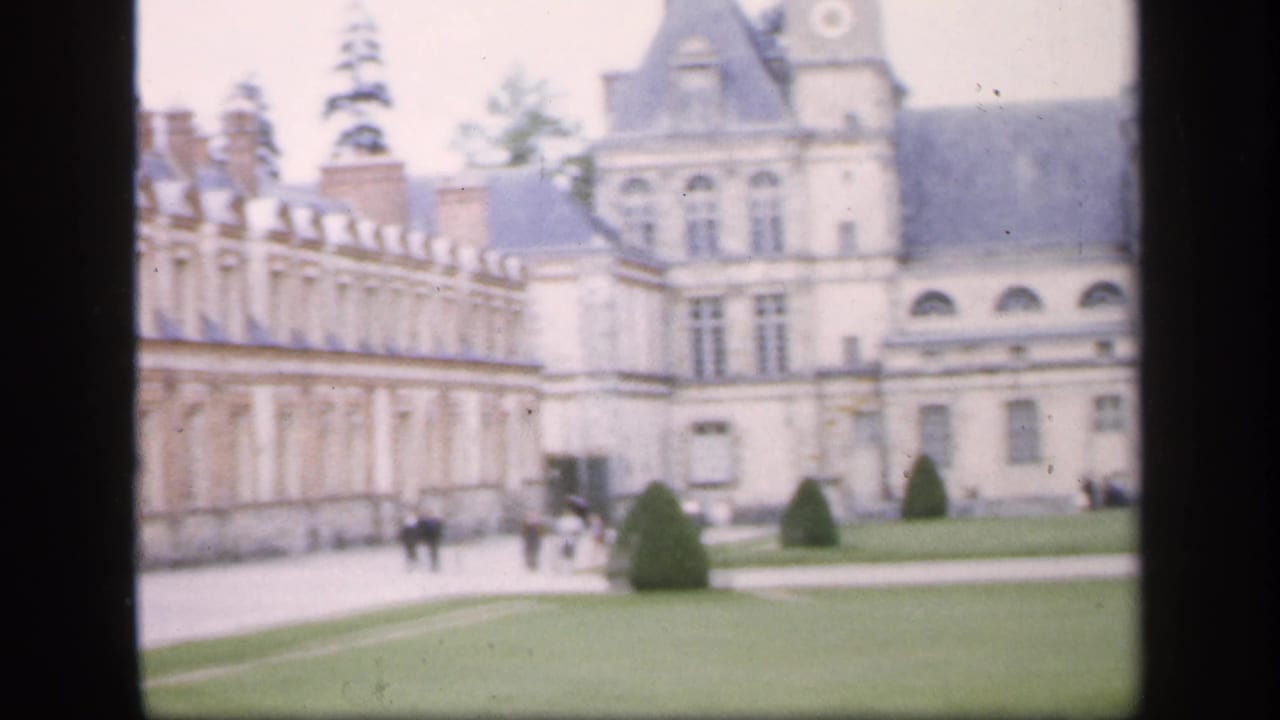 1949 Ireland travel footage frame with an ornate palace wing, arched lower windows, clipped shrubs, lawn paths, and small visitor figures.