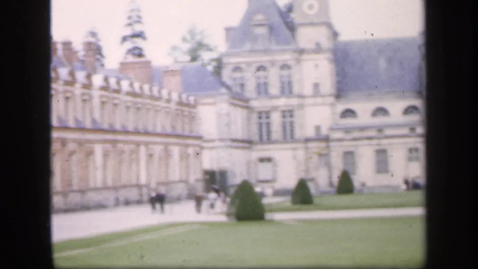 1949 Ireland travel footage frame with an ornate palace wing, arched lower windows, clipped shrubs, lawn paths, and small visitor figures.