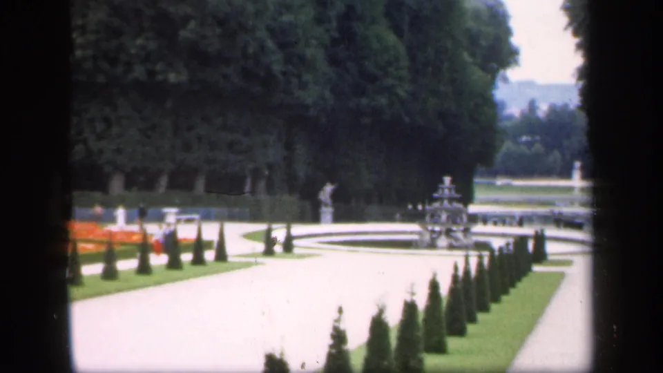 1949 Ireland garden view showing curving pale paths, conical hedges, fountains, lawns, trees, and small distant visitors.