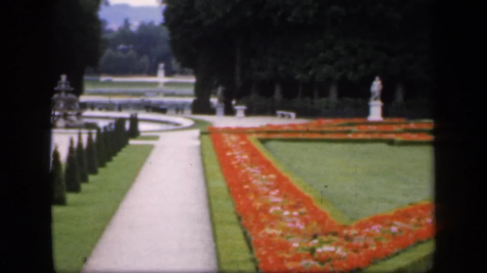 1949 Ireland formal garden view with a straight path, red flowerbed borders, trimmed green lawns, hedges, trees, and a white statue.