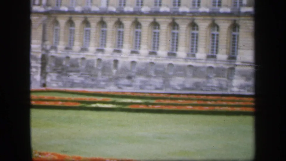 1949 Ireland 8mm frame showing a pale stone facade with repeated arched windows, red flower borders, and a broad lawn.
