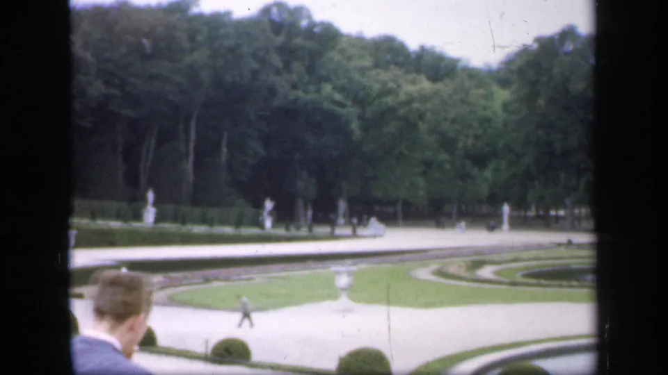 1949 Ireland 8mm frame of formal garden paths and trees, with white statuary and a visitor partly visible at the lower edge.