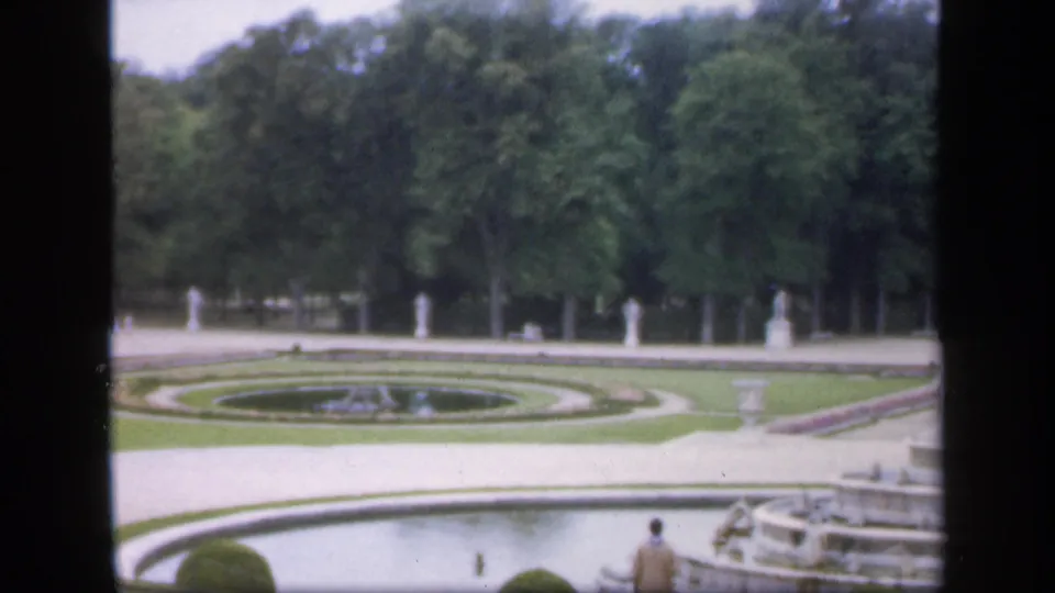 1949 Ireland home-movie frame with a pond or basin in front, circular formal lawns beyond, dense trees, statues, and a tiered fountain at right.