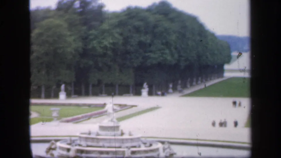 1949 Ireland garden scene with a central fountain, geometric paths, lawns, statues, dense trees, and visitors walking in the distance.