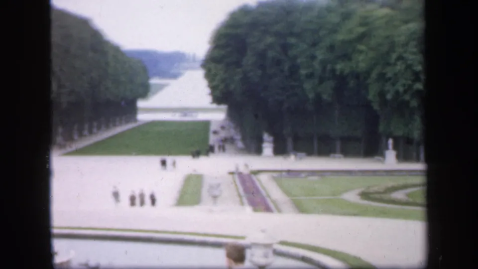 Soft 8mm frame of a formal Irish garden in 1949, with broad paths, statues, clipped lawns, flowerbeds, and distant pedestrians.