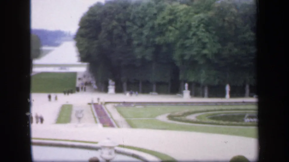 1949 Ireland home-movie frame of formal garden grounds, showing trees, paths, statues, lawns, visitors, and a fountain or basin below.