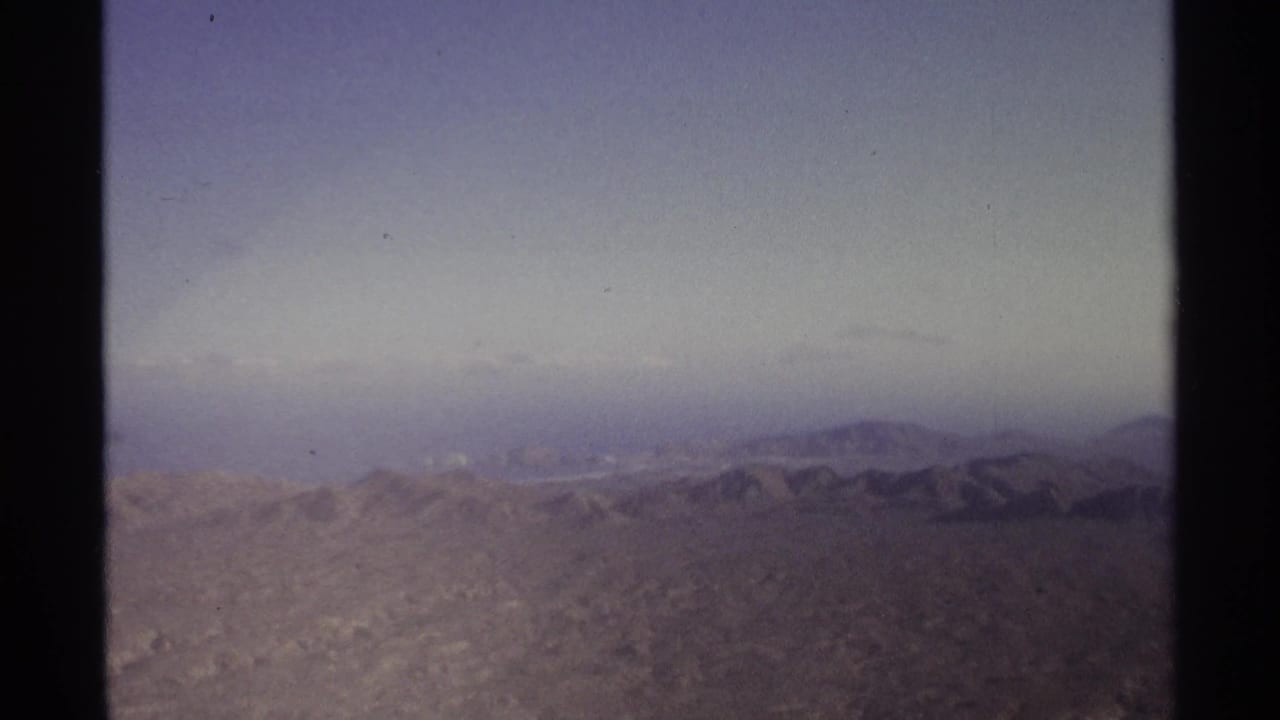 Hazy desert mountain ridges under a pale sky with film gate edges visible.
