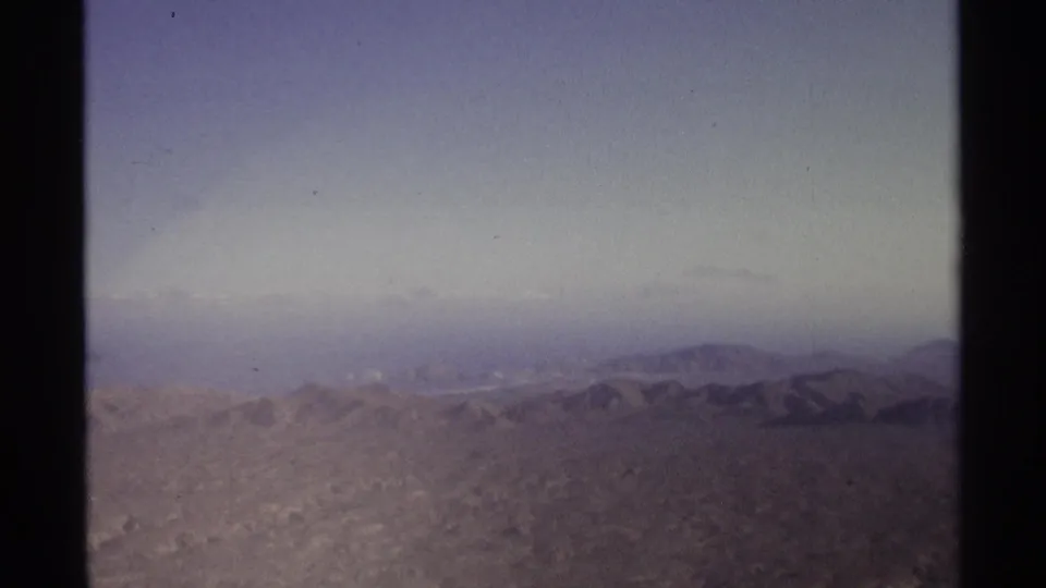 1974 8mm view near Cabo San Lucas showing arid mountain ridges beneath a hazy purple-blue sky.