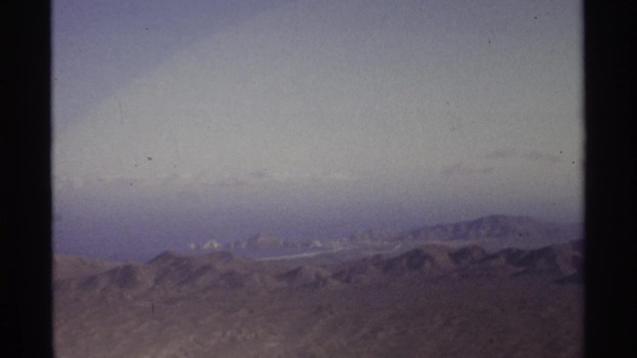1974 8mm frame near Cabo San Lucas with low desert mountains and a faint distant coast through haze.