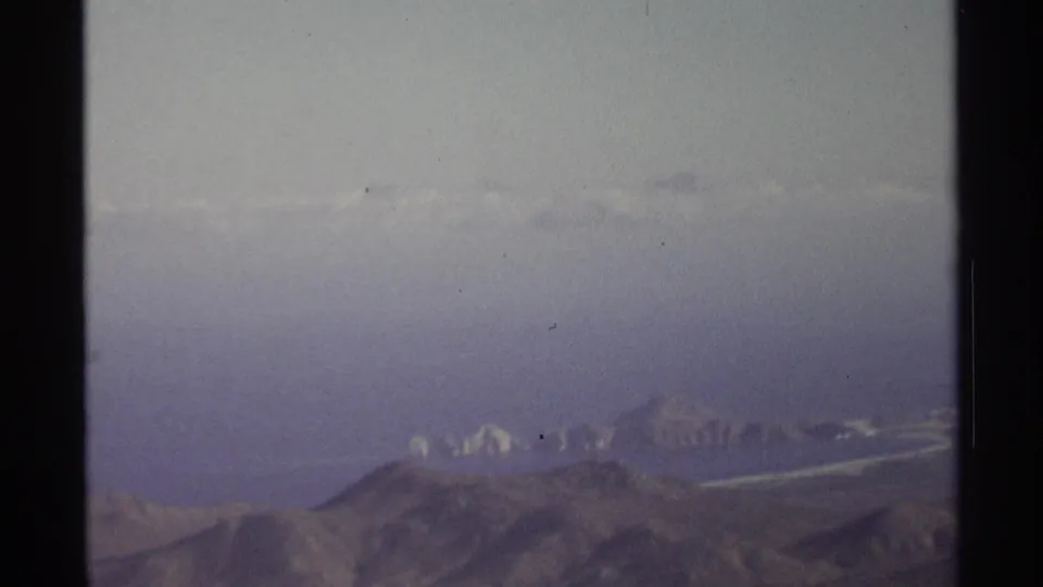 1974 8mm coastal-desert view near Cabo San Lucas with ridges, haze, and faint shoreline details.