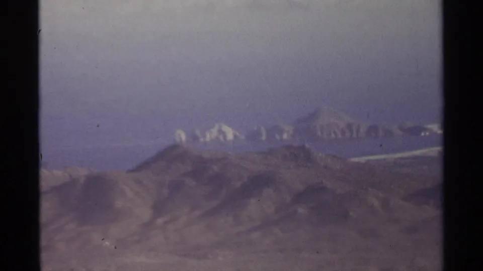 1974 Cabo San Lucas home-movie frame showing hazy mountain ridges and dry terrain from an aerial viewpoint.
