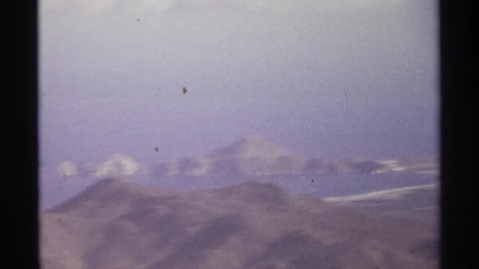 Soft 1974 Cabo San Lucas aerial frame showing dry hills and bright distant ridges through 8mm grain.