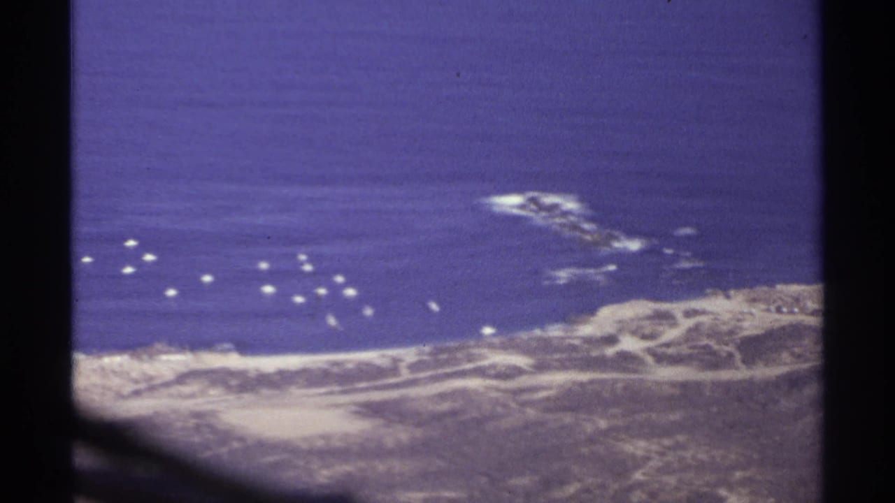 Aerial coastline view through airplane window with blue ocean and white surf below.