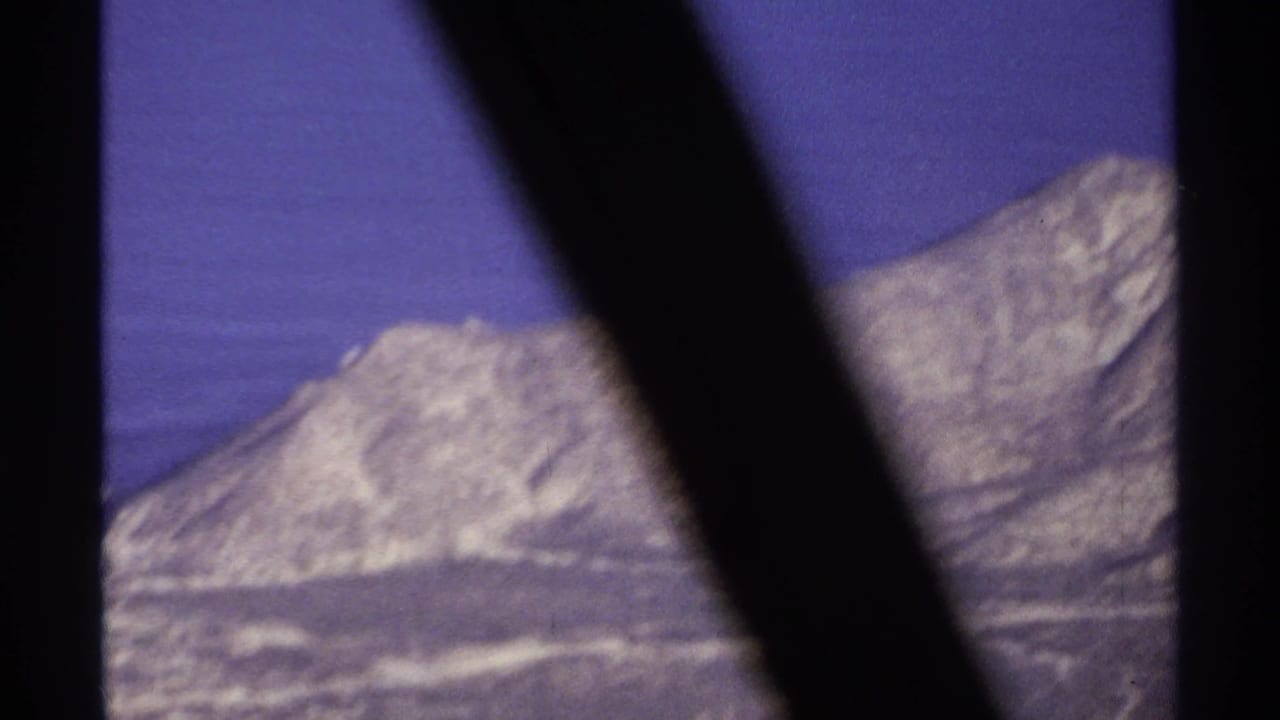 Distant pale mountain ridge under a blue-purple sky, partly blocked by dark diagonal foreground shapes.
