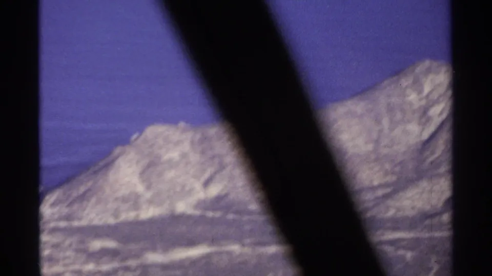 1974 8mm travel frame from Cabo San Lucas metadata showing a distant rugged ridge through dark foreground bars or window framing.