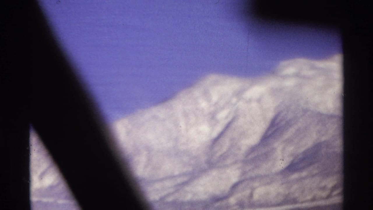 Rugged mountain peaks beneath a blue-purple sky, framed by dark vertical and diagonal shapes.