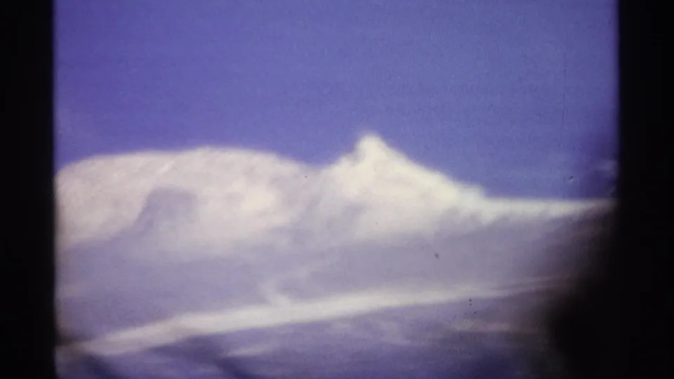 1974 8mm travel frame showing a bright snowy mountain ridge, soft exposure, and blue sky within the film gate.