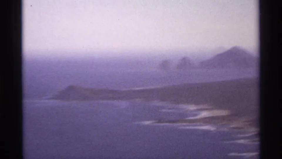 1974 Cabo San Lucas home-movie frame with a soft view across blue water toward low coast and distant rocky formations.