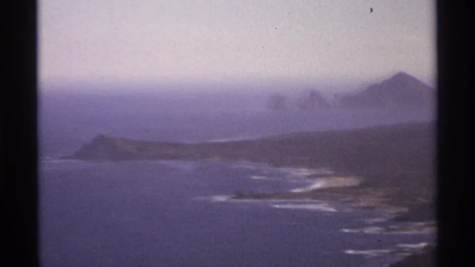 8mm Cabo San Lucas coastal panorama with rocky shore, blue water, white surf traces, distant hills, and visible film gate edge.