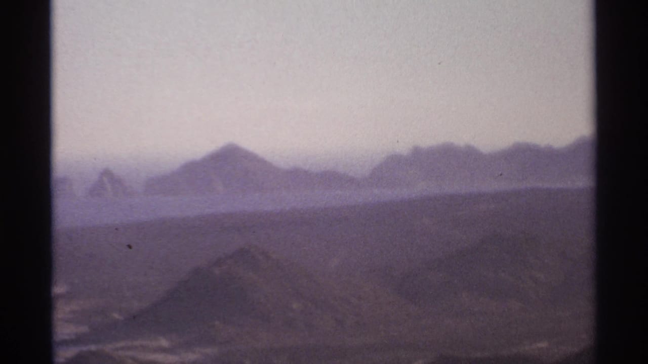 1974 Cabo San Lucas home-movie frame showing hazy mountain ridges and distant ocean through dark 8mm frame borders.