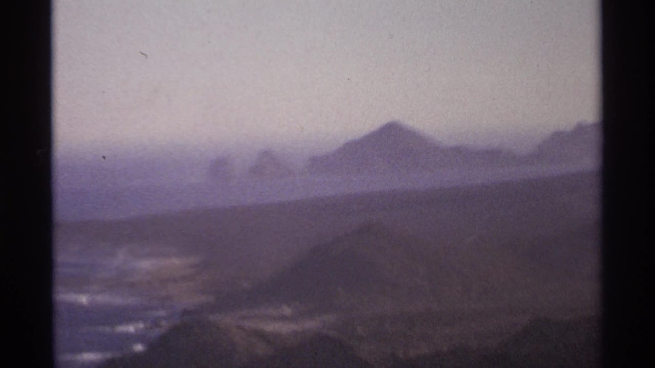 Mountain range and shoreline under a pale hazy sky.