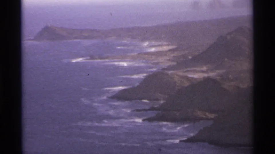 1974 home-movie view of rocky Cabo San Lucas headlands with surf lines and ocean stretching along the coast.