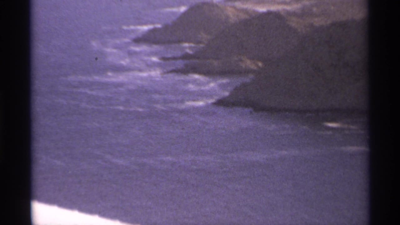 Rocky coastal headlands with ocean waves and dark 8mm film borders.