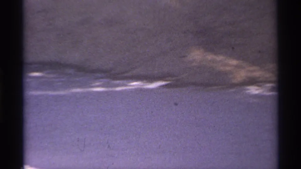 A low rocky coast and waterline appear in this 1974 Cabo San Lucas 8mm frame with grain and purple fading.