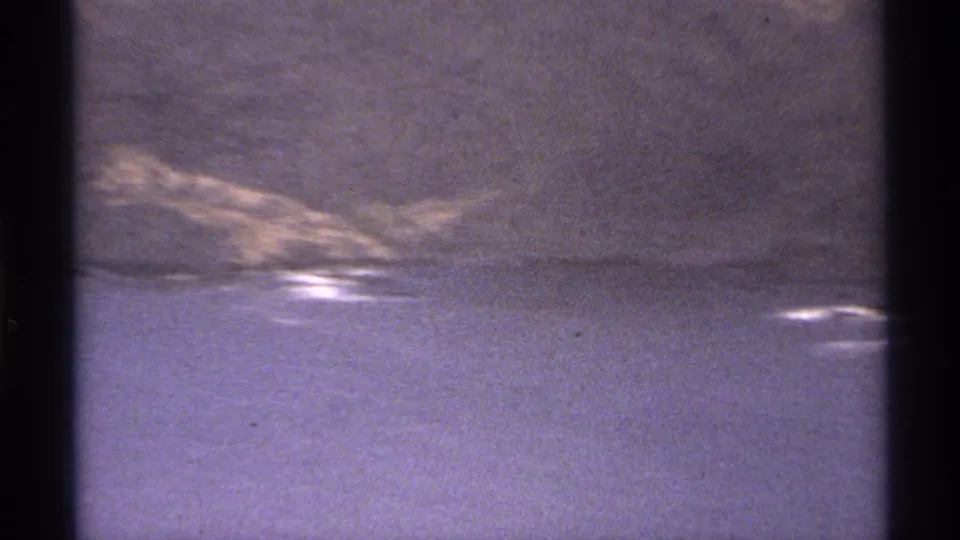 Final 1974 Cabo San Lucas 8mm frame showing ocean surf, low rocks, and soft aged-film color shift.